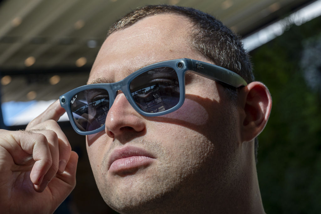 A close up of a man with dark hair wearing large black sunglasses that have a camera on them