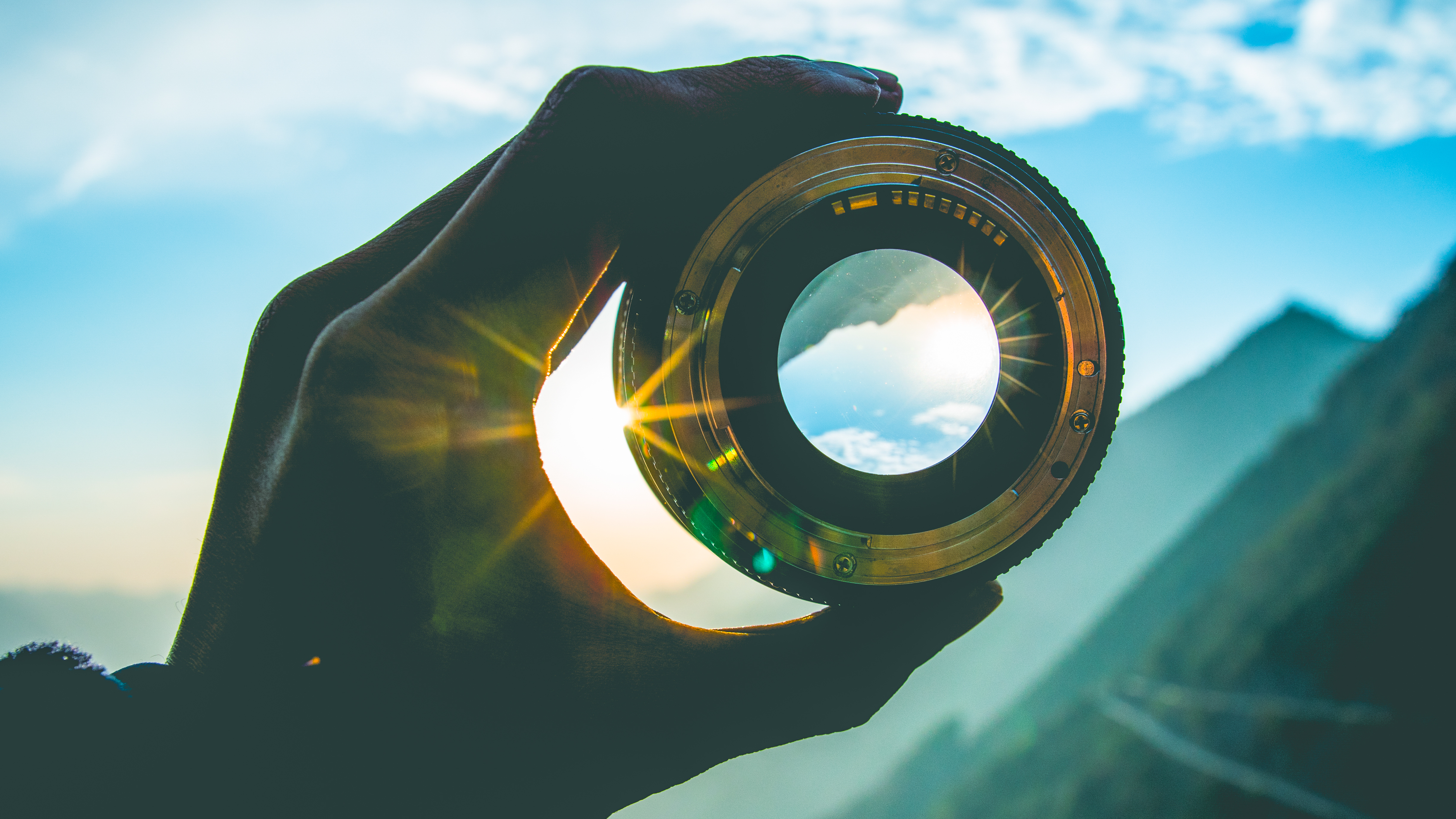 Hand holding up lens in front of mountain scene at sunset