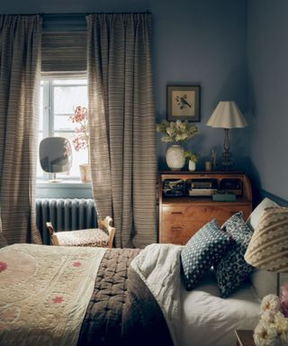 bedroom with muted blue walls, cozy decor and patterned blue cushions