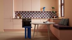 peach kitchen cabinets with checkerboard tiled backsplash, timber floorboards, timber countertop, built-in bench seat with round timber dining table with blue stool