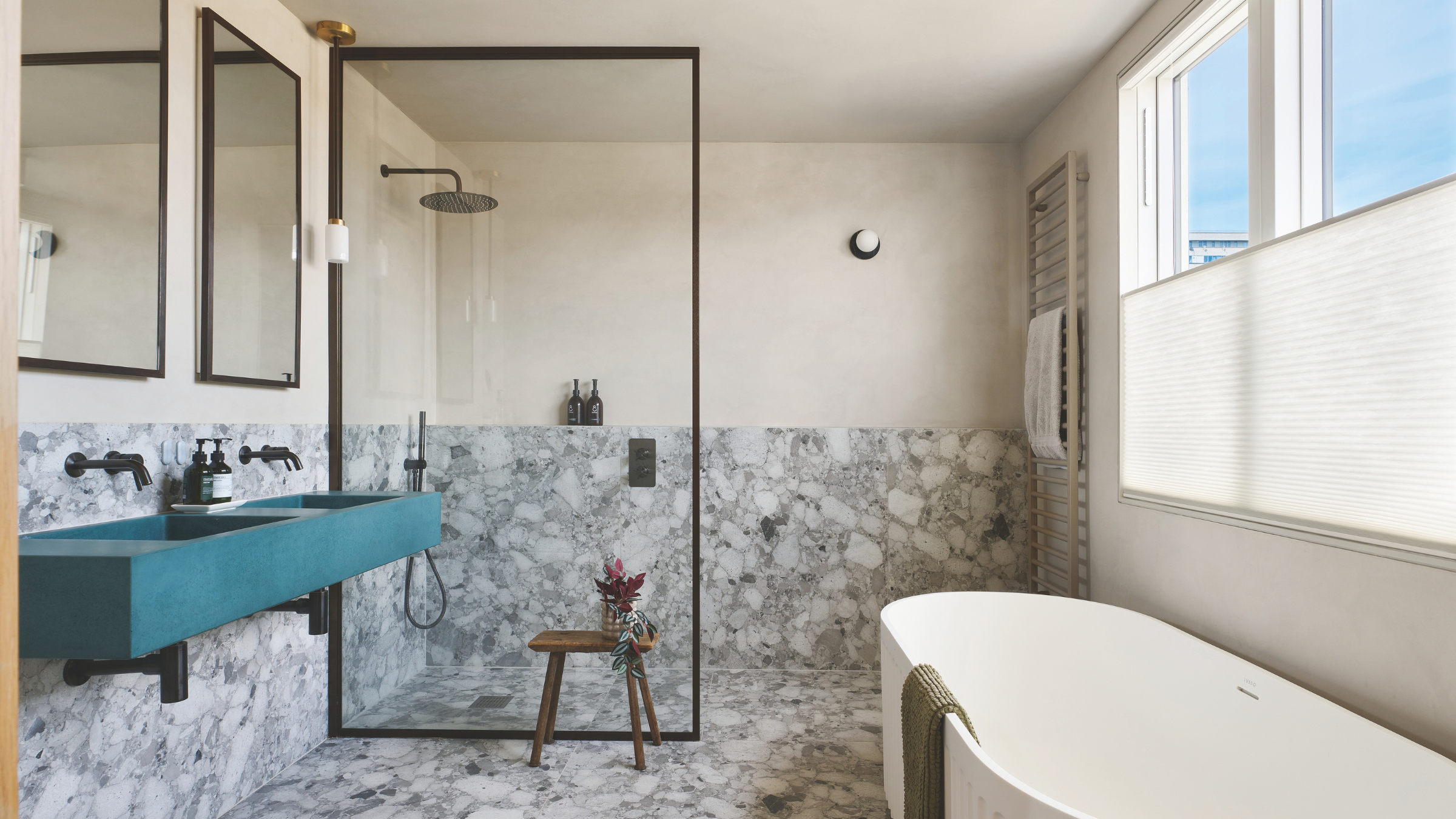 Freestanding bath and seperate shower in grey tiled bathroom with teal sink.