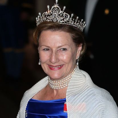 Queen Sonja of Norway wears a royal blue dress, a white shawl, and a diamond tiara