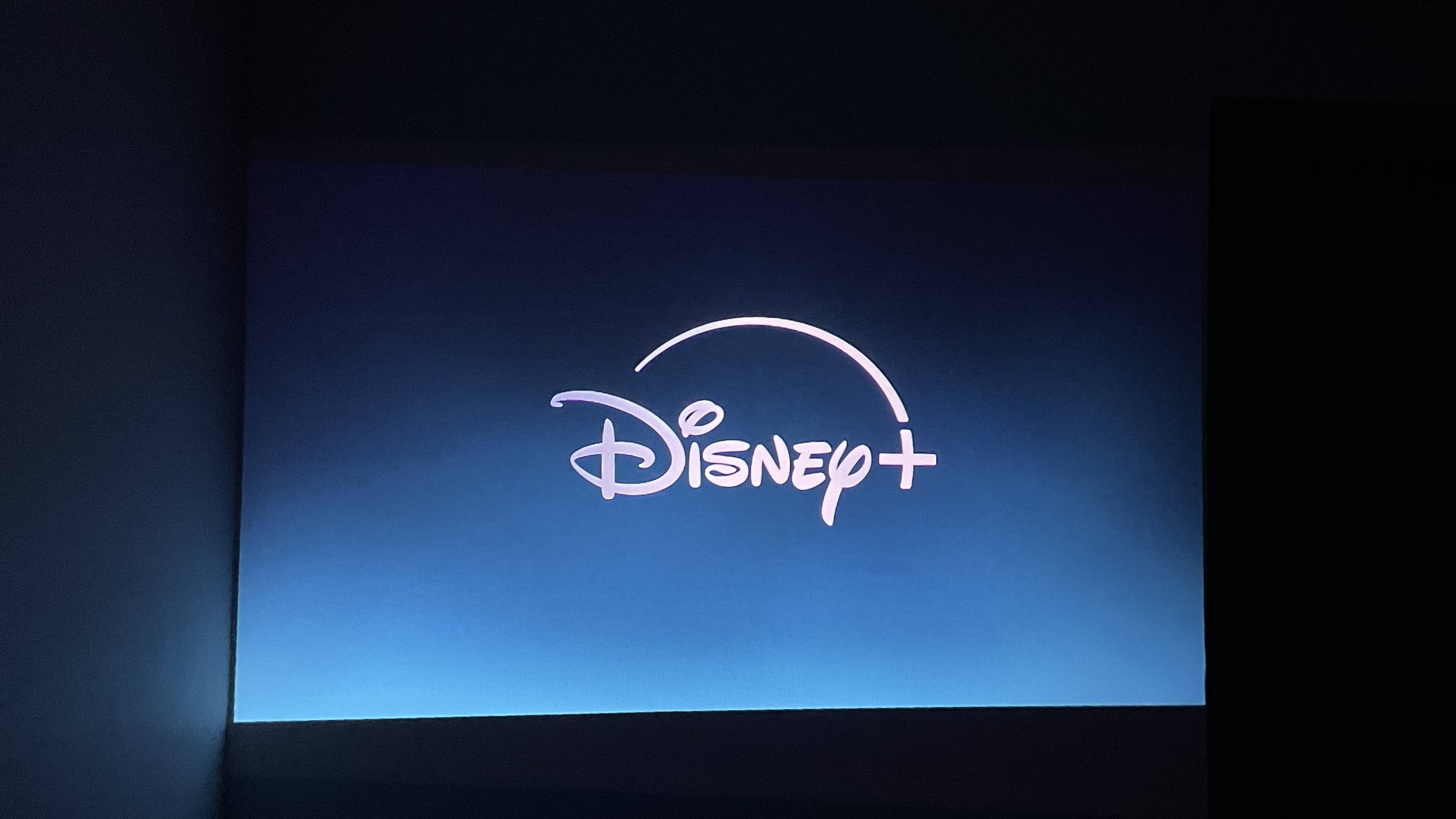 The Disney Plus app title page is projected onto a wall in a dark room.