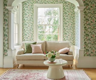 delicately patterned pink and green floral wallpaper on living room walls with netural sofa in large bay window
