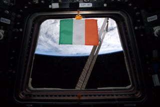 To honor St. Patrick's day at the International Space Station on March 17, 2020, NASA astronaut Andrew Morgan tweeted this photo of an Irish flag floating in one of the windows of the Cupola observatory in the orbiting lab. One of the space station's solar arrays is visible through the window, while Earth provides a cloudy backdrop. Along with this photo of the flag, Morgan tweeted a photo of Ireland, also known as the Emerald Isle, that he captured from the space station.
