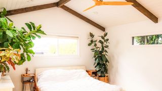 A bed is placed in a white and neautral bedroom setting under a sloping ceiling and exposed beams