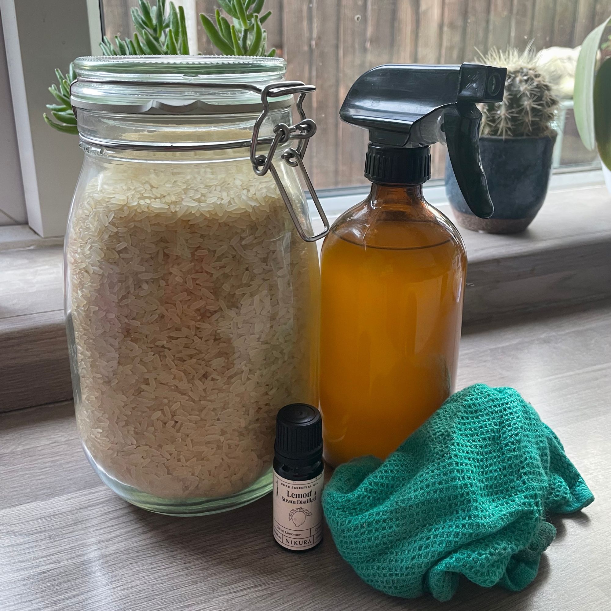 Jar of rice next to a bottle of rice water, a small bottle of lemon essential oil and a green cleaning cloth