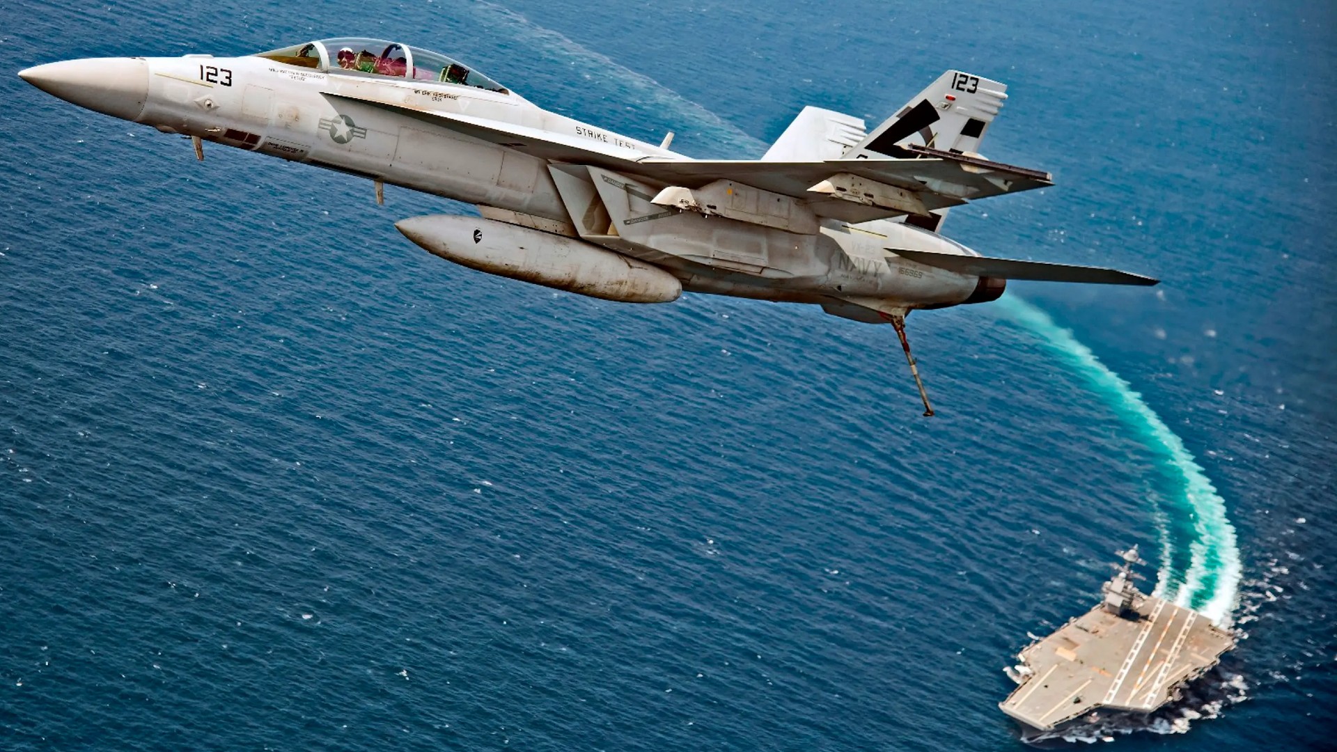 a fighter jet lifts off from the surface of an aircraft carrier at sea