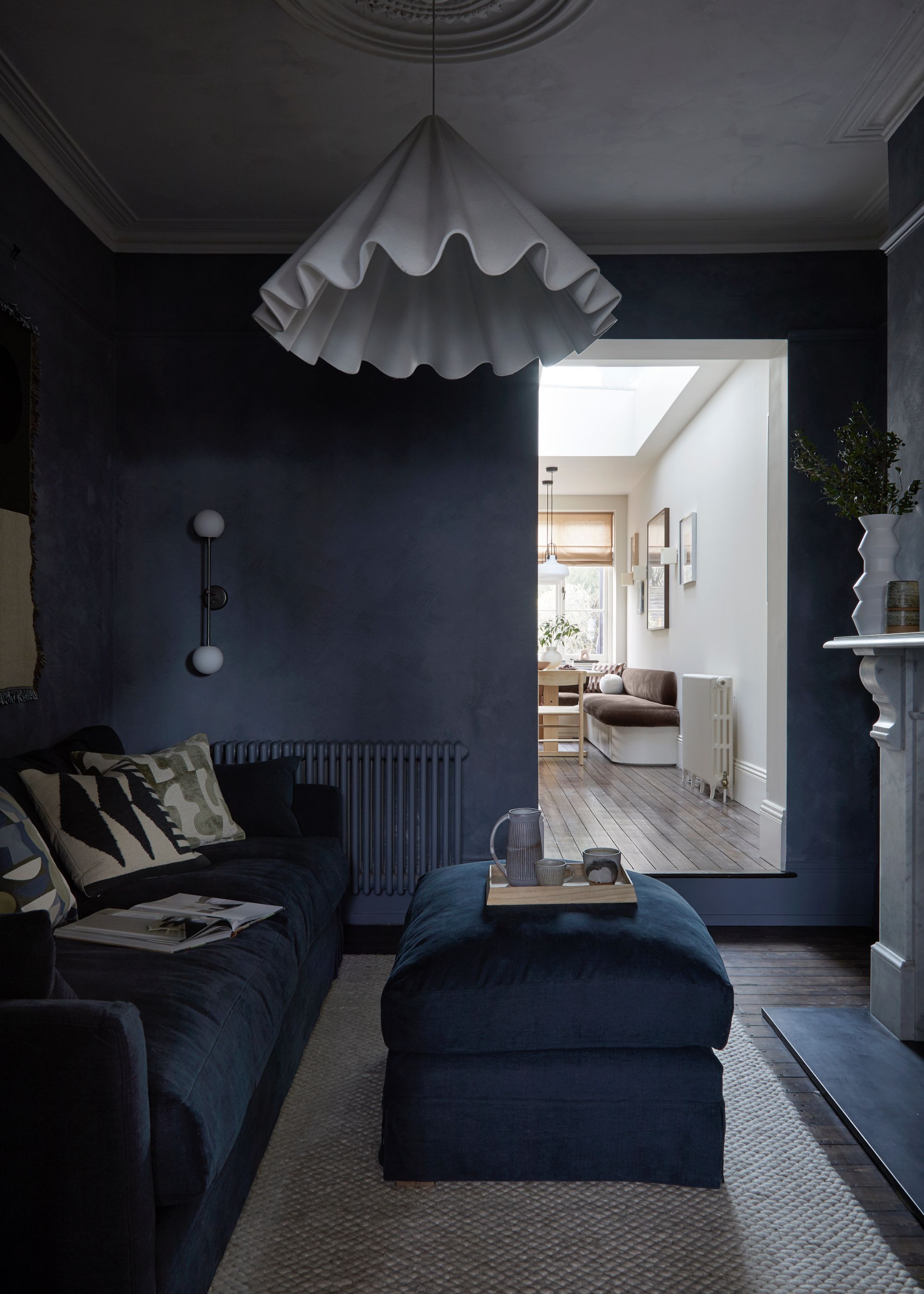 dark living room with navy walls, navy sofa and footstool and white pendant light