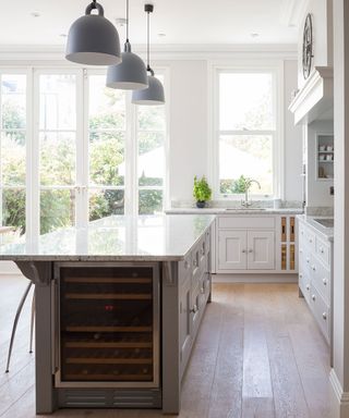An open plan kitchen with marble worktops and an island with gray cabinets and a wine cooler