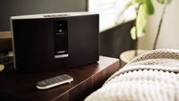 A Bose SoundTouch 20 speaker on a bedside table with its remote control.