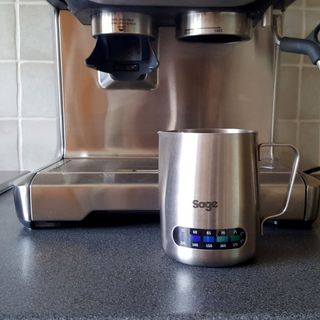 The stainless steel milk jug with temperature indicator that comes with the Sage Barista Express coffee machine