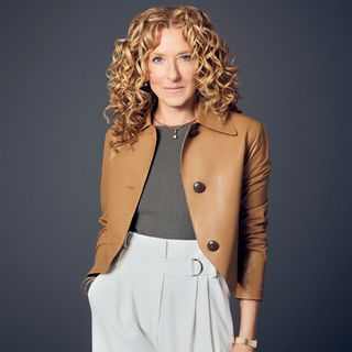 Kelly Hoppen wearing a brown leather jacket, grey shirt tucked into white trousers