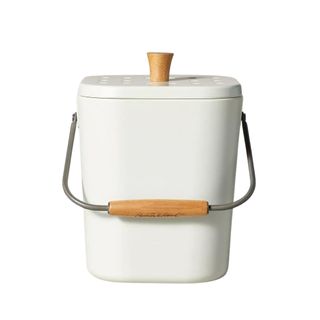 A white rectangular compost bin with a metal handle with a wooden grip and a wooden handle on top of the lid