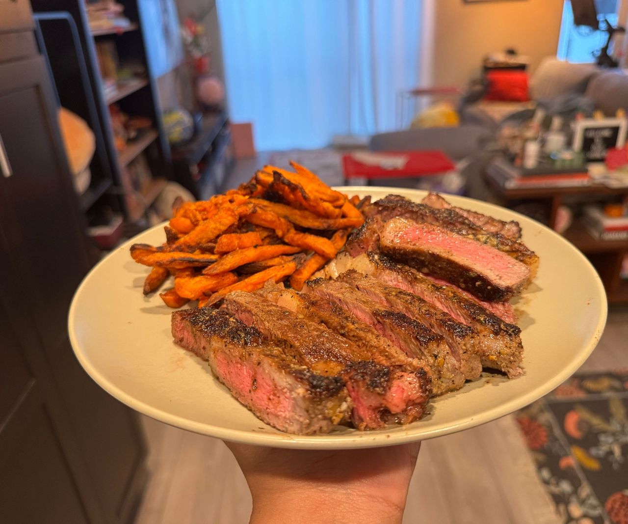 A plate of sliced medium rare steak, and sweet potato fries