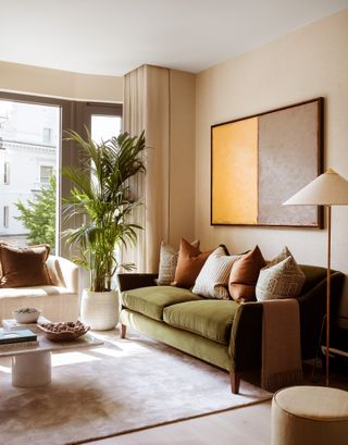 neutral living room with green sofa, rust and patterned cushions, painting on wall, paint, floor lamp, drapes