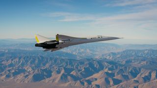 a sleek silver jet with a sharp nose cone flies above a mountain range