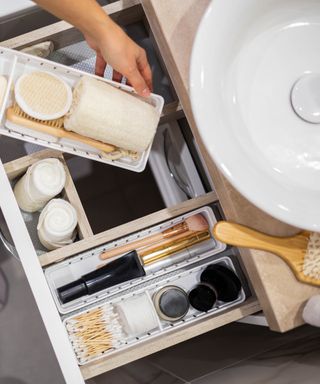 An image of a bathroom drawer open by a sink with storage trays and products neatly organized