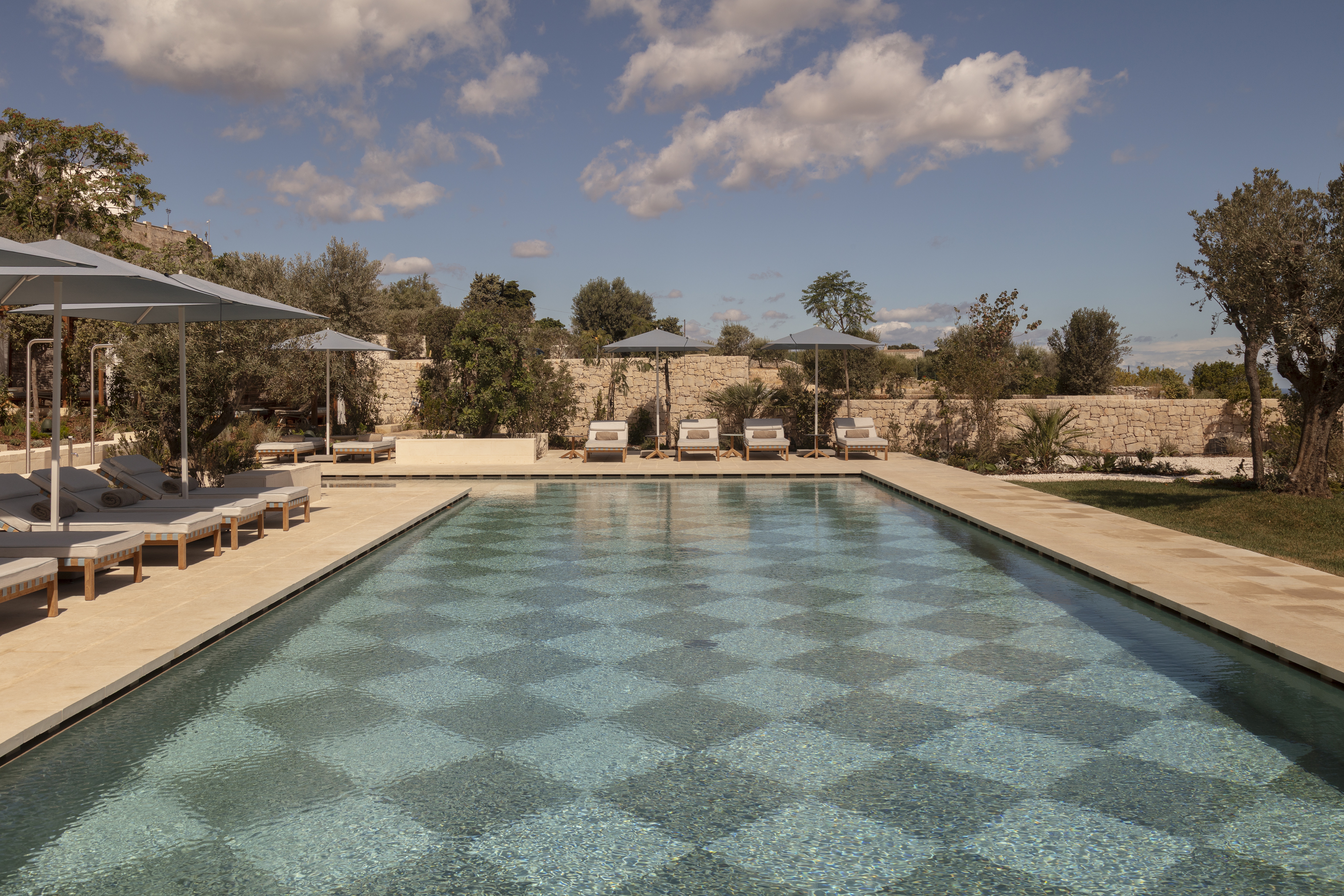 A checkered pool with minimal parasols and loungers, caught under the sun.