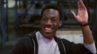 Eddie Murphy waves while smiling in a warehouse in Beverly Hills Cop.