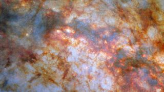 A close-in view of the centre of galaxy M82. Bright, bluish light radiating from the centre is due to stars actively forming there. A thick lane of gas, black in the centre and red around the edges, crosses the centre and blocks much of the light. Thinner strands and clumps of reddish dust cover much of the rest of the view.