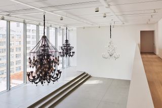 One of the rooms with panoramic windows at the Pace gallery. Three extravagant chandeliers are hanging from the ceiling. Two are black and one is white.