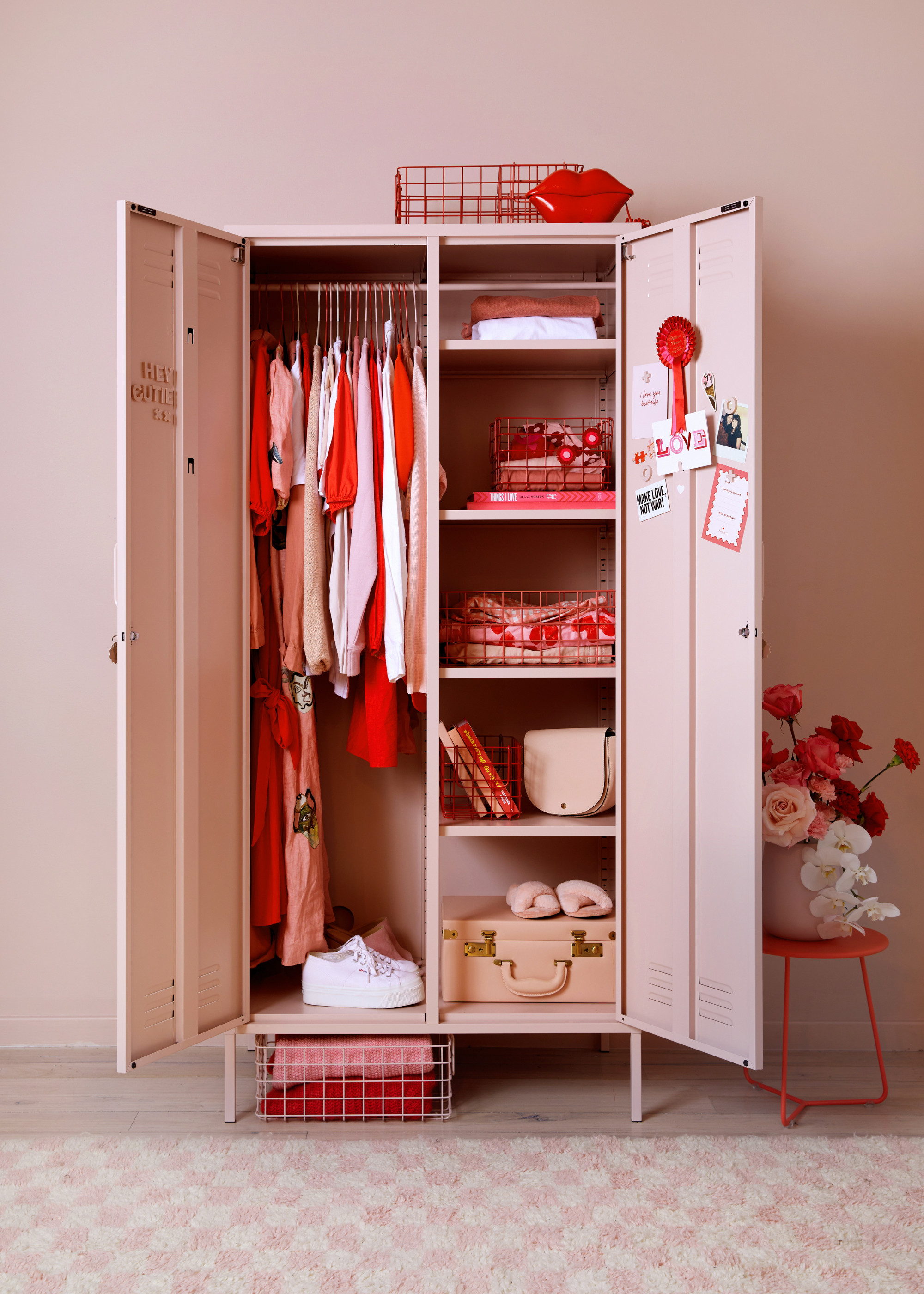 A bright bedroom with a blush pink and hot red color scheme, an open wardrobe locker and red wire baskets for storage
