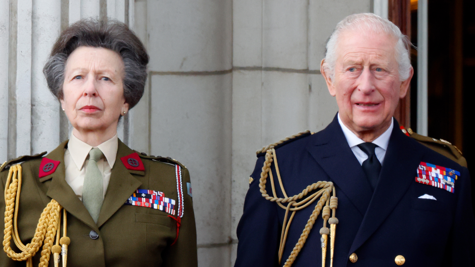 Princess Anne wears an olive green military uniform and stands with brother King Charles, who wears a navy naval uniform