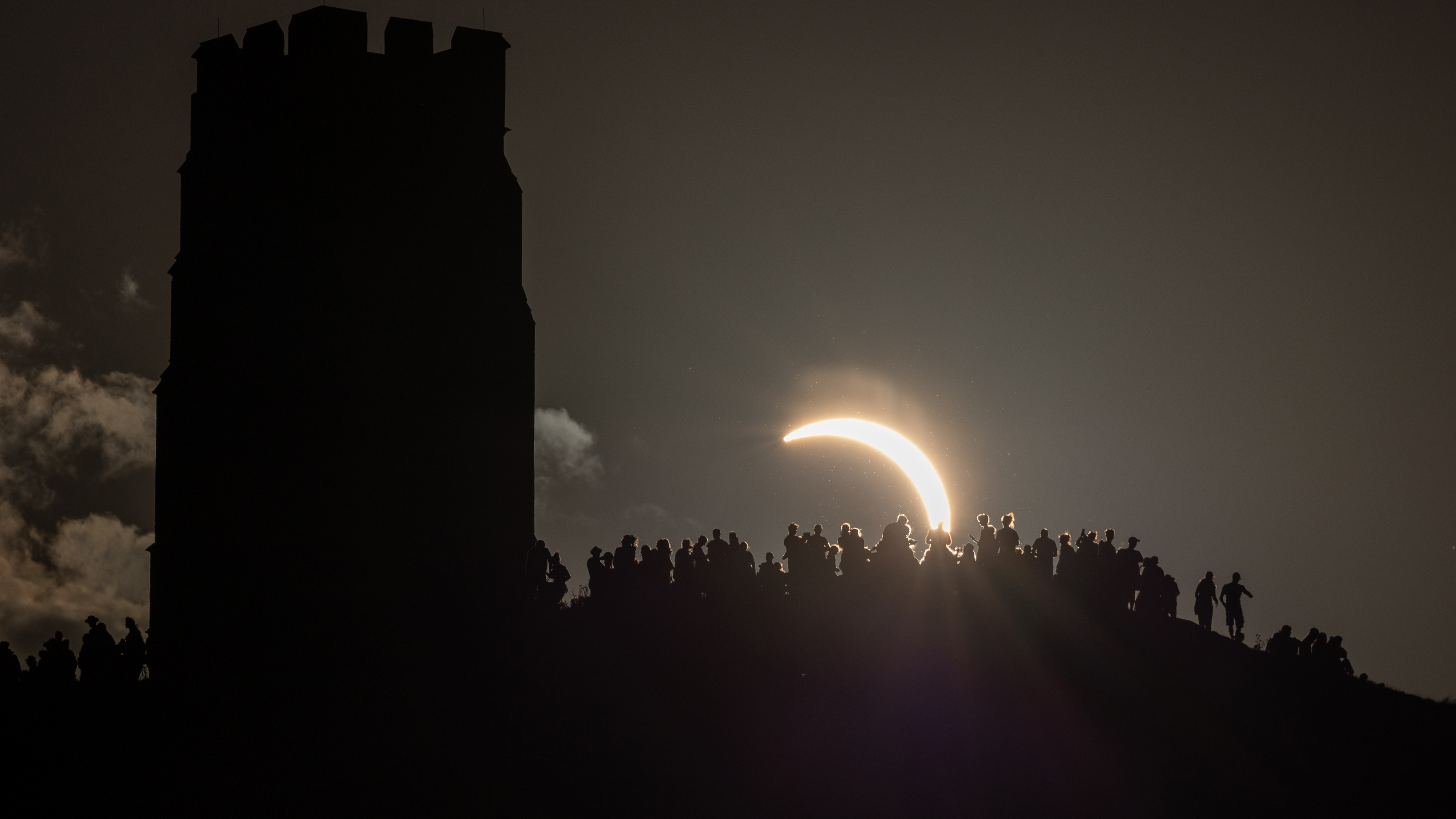 GLASTONBURY, ENGLAND - AUGUST 12: People view the partial solar eclipse from besides the historic St. Michael's Church tower, a Grade I listed building at the top of Glastonbury Tor on August 12, 2026 in Glastonbury, England. The partial solar eclipse is the most coverage during an eclipse viewed from the UK since 1999, with the moon covering 90-96% of the sun. (Photo by Matt Cardy/Getty Images)