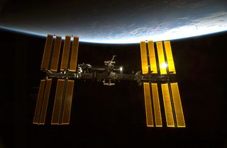 Sunlight glints off the International Space Station, with the blue limb of Earth providing a dramatic backdrop.