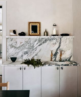 Neutral home bar design featuring a marble counter top and backsplash and brass hardware