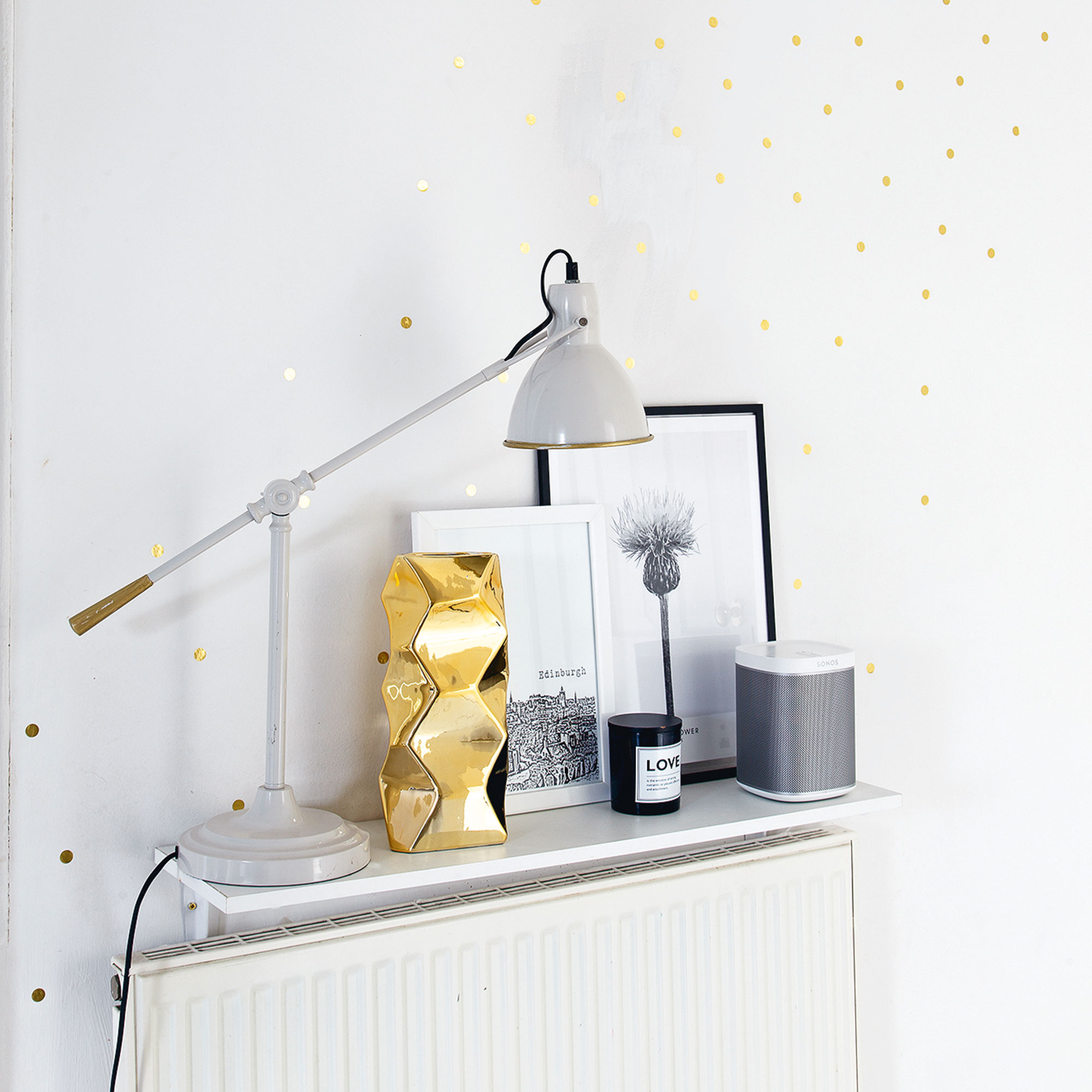 Radiator shelf over a radiator against a white wall decorated with a lamp, vase and candle