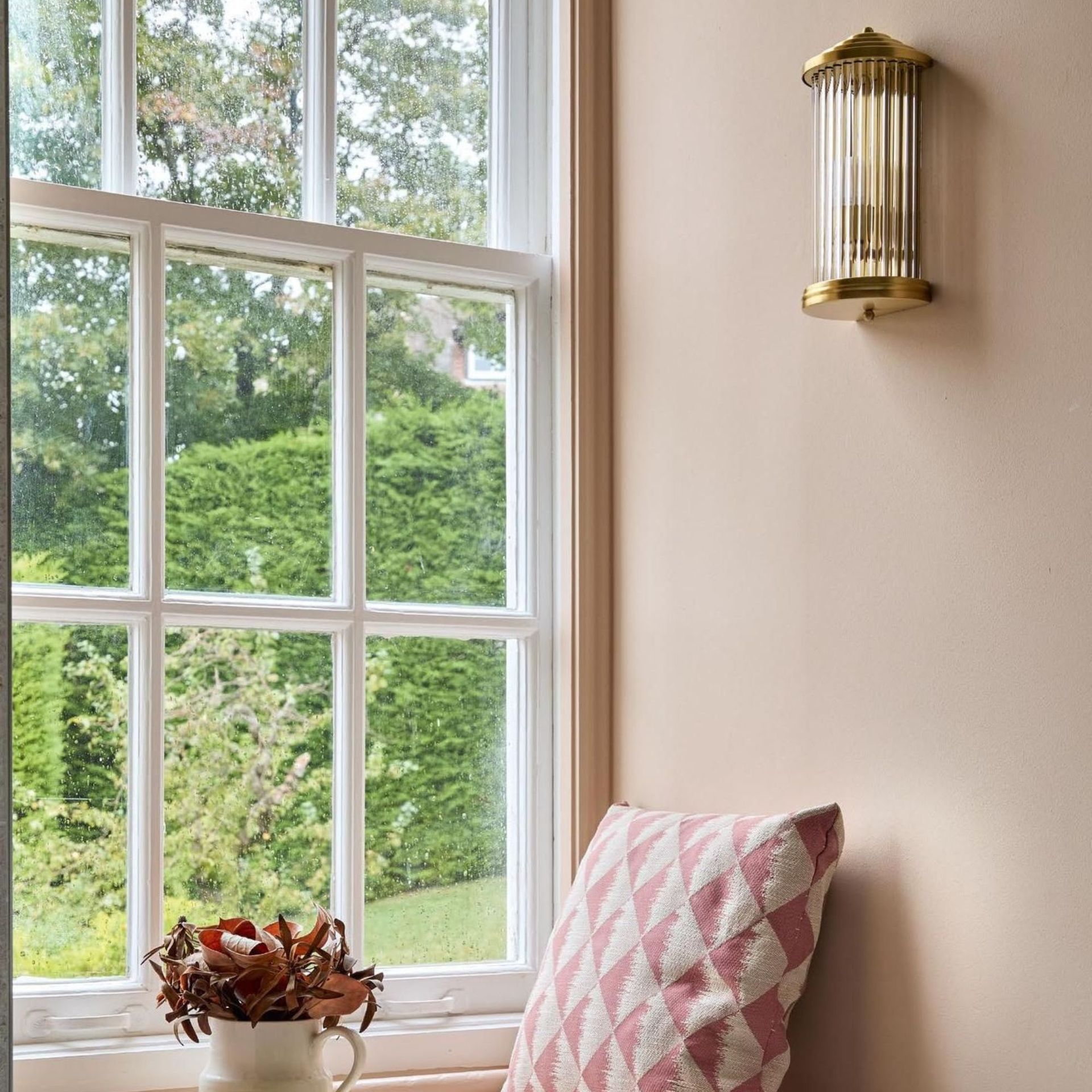 Bathroom window seating with pale pink walls, wall light and cushion