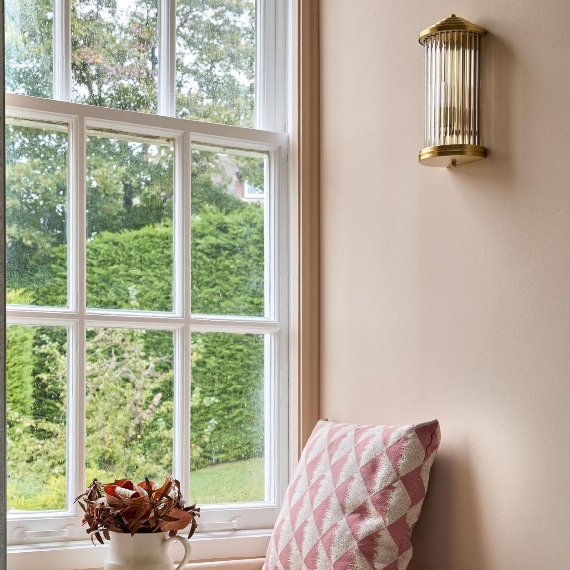 Bathroom window seating with pale pink walls, wall light and cushion