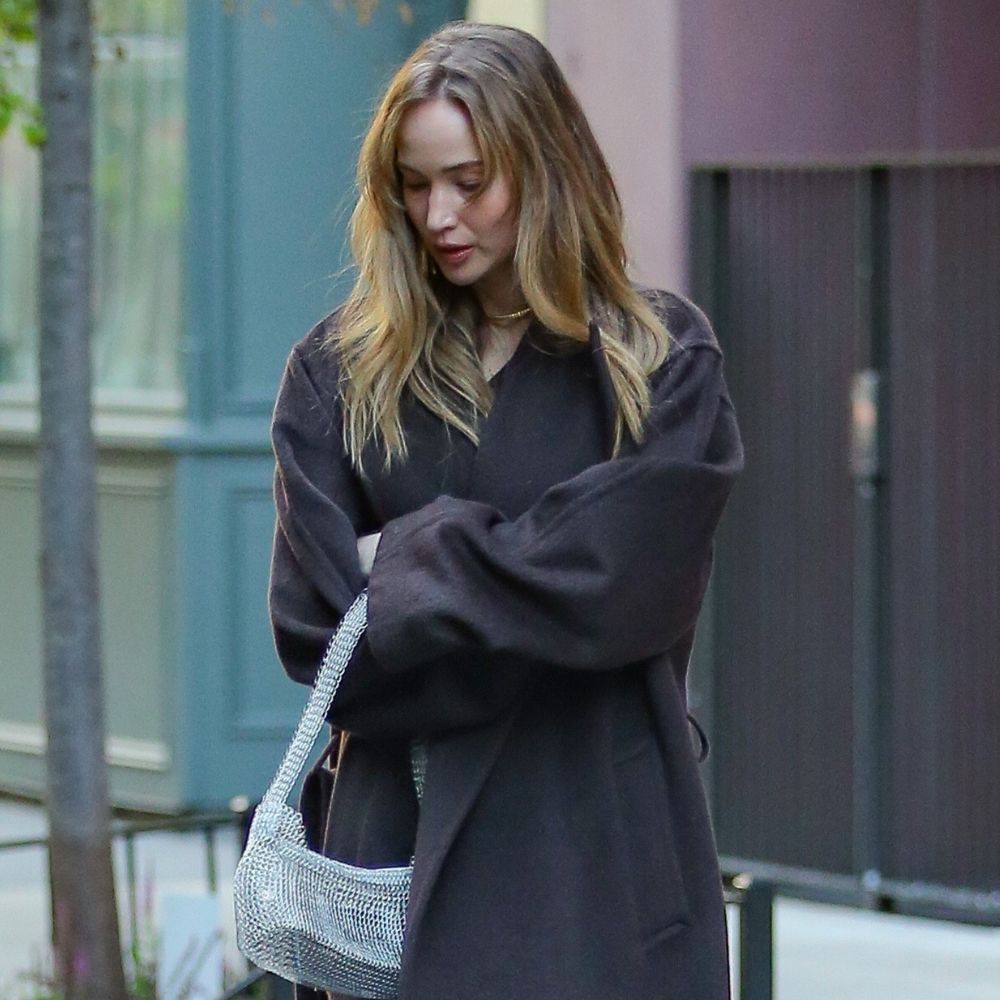 Jennifer Lawrence wears black satin kitten heels with a brown coat and a silver sparkly bag.