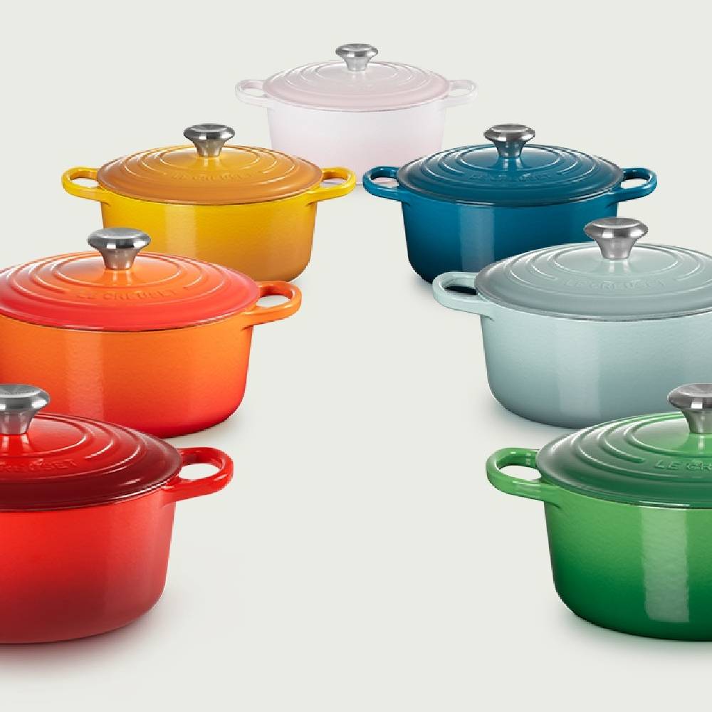 Seven Le Creuset cast iron casserole dishes in various rainbow colours.