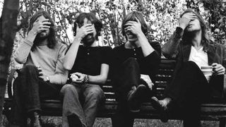 Pink Floyd seated on a park bench, covering their eyes
