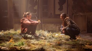Ellie (Bella Ramsey) and Tess (Anna Torv) sit together on a mossy mound in The Last Of Us