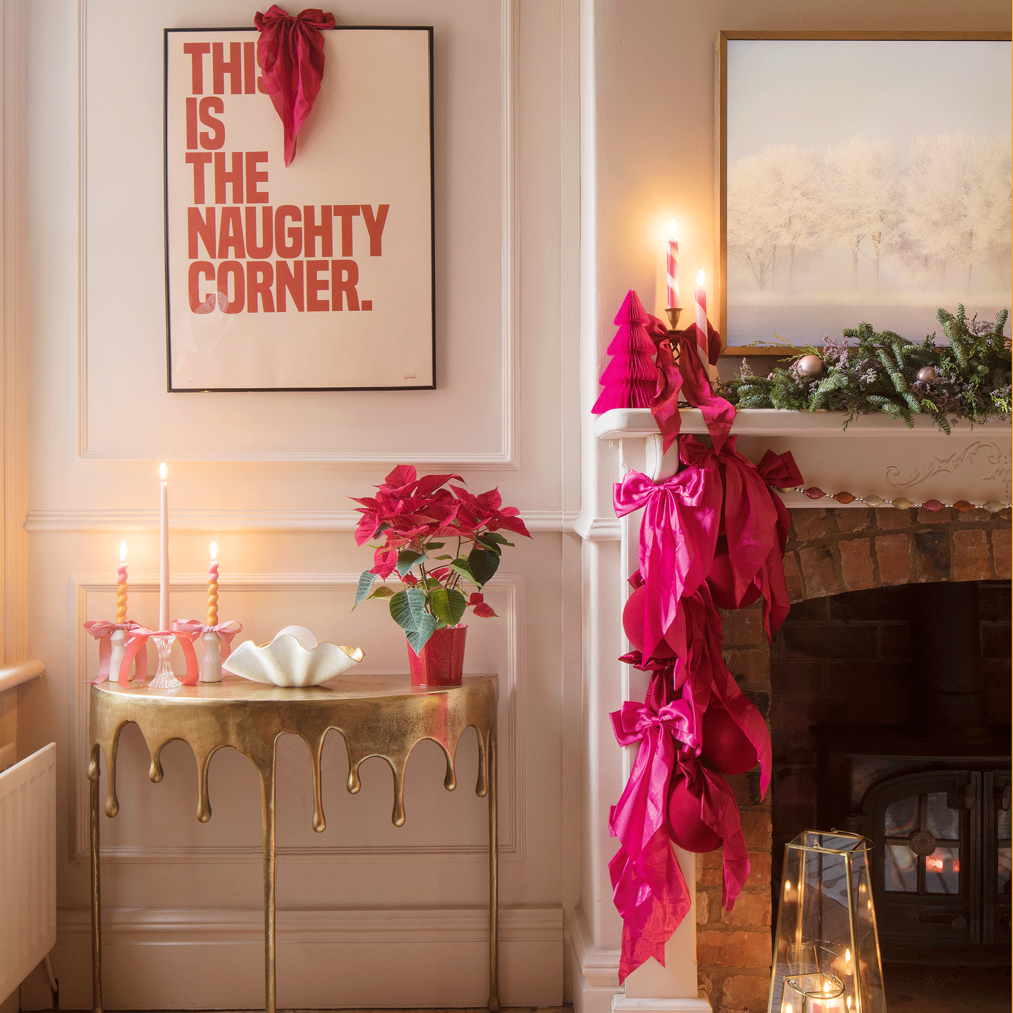 a living room with a mantelpiece with festive greenery, candles, a bold pink paper Christmas tree and plenty of bows, a gold statement console table and bold typography artwork above