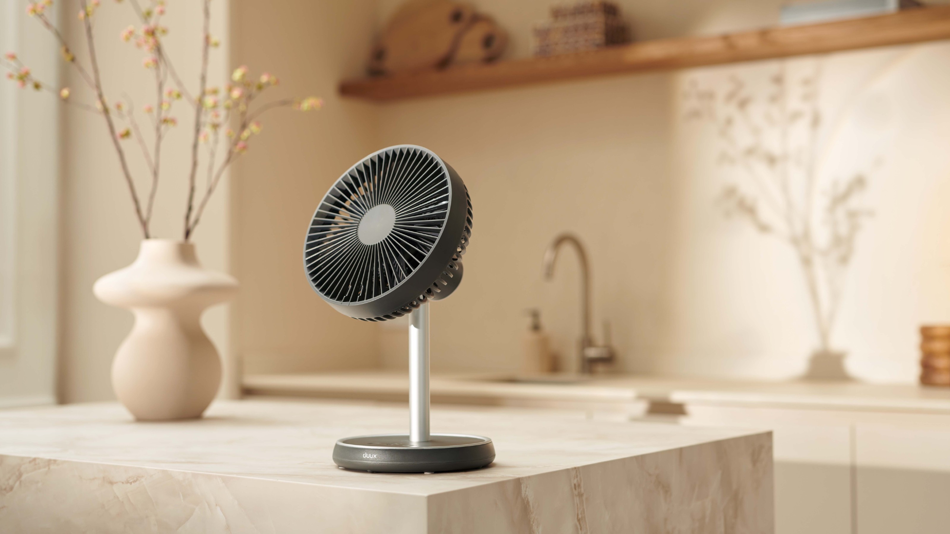 Charcoal grey Duux Rize fan in desktop configuration on a marble kitchen island in a neutral kitchen