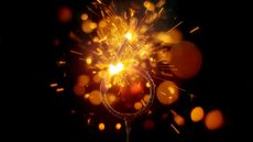 Close-up of sparkler in shape of 'NUMBER 6' emitting sparks while burning against black background