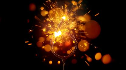Close-up of sparkler in shape of 'NUMBER 6' emitting sparks while burning against black background