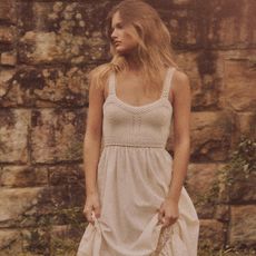 model wears white dress while gathering the skirt and looking off into the distance
