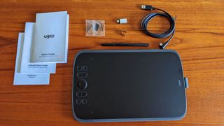 Ugee M908 review; a black small drawing tablet on a table with accessories