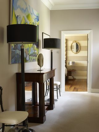 Lading with neutral walls and carpet, console table, two side chairs, two floorstanding lamps and artwork on wall