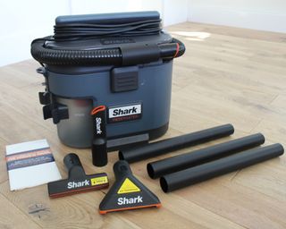 Shark MessMaster vacuum cleaner with a crevice tool, a squeegee tool, and a rug tool on laminate floor