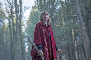 kiernan shipka as sabrina walking through the woods in a red cloack in The Chilling Adventures of Sabrina