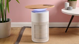 The SwitchBot Air Purifier Table is pictured in a pink living room. The ambient light below the tabletop is lit up blue.