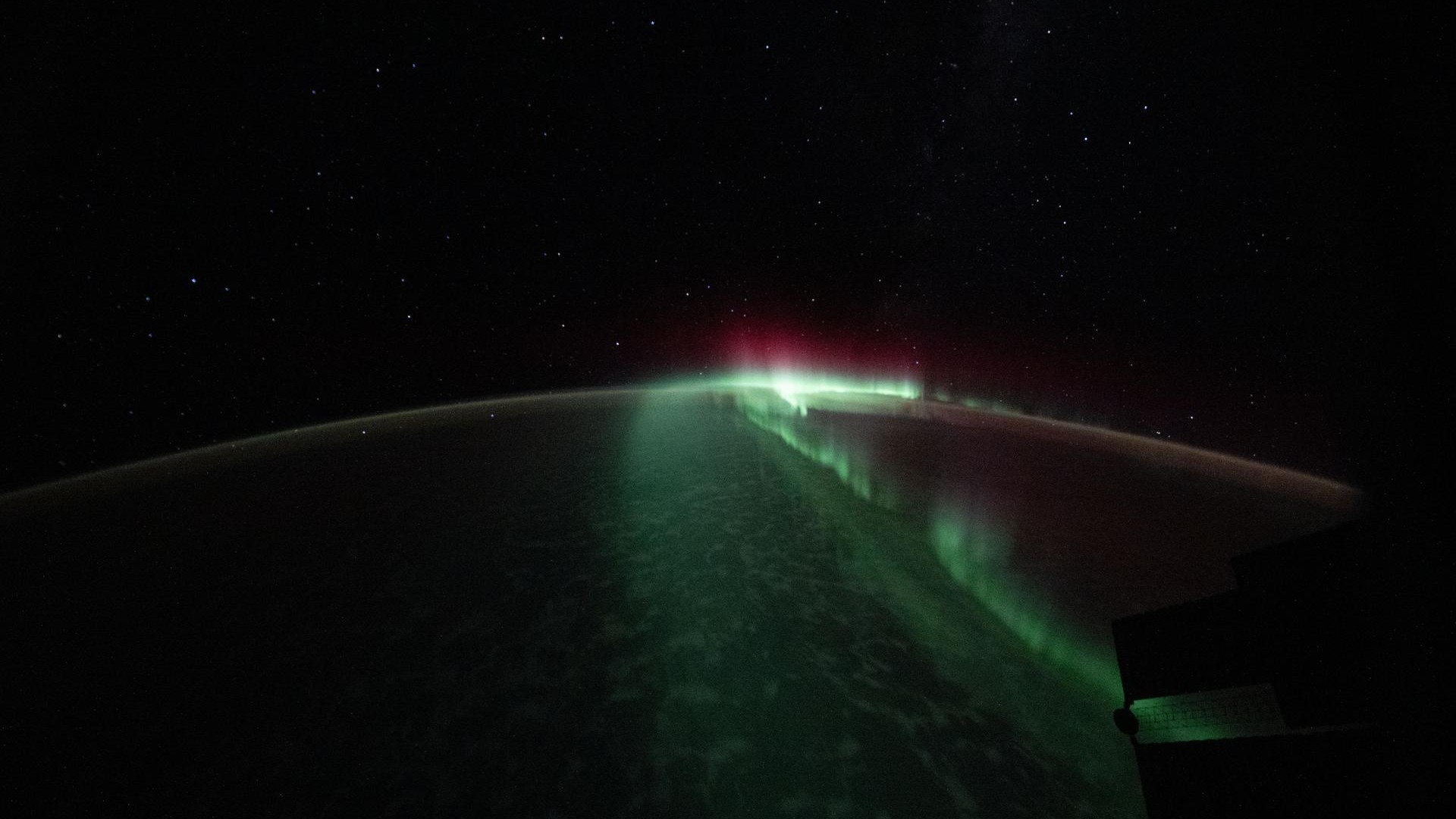 The curve of the Earth against space is highlighted by a bright green streak of light down the middle with some pink light near the top. 
