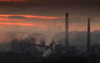 Smoke rises from an industrial building during sunset